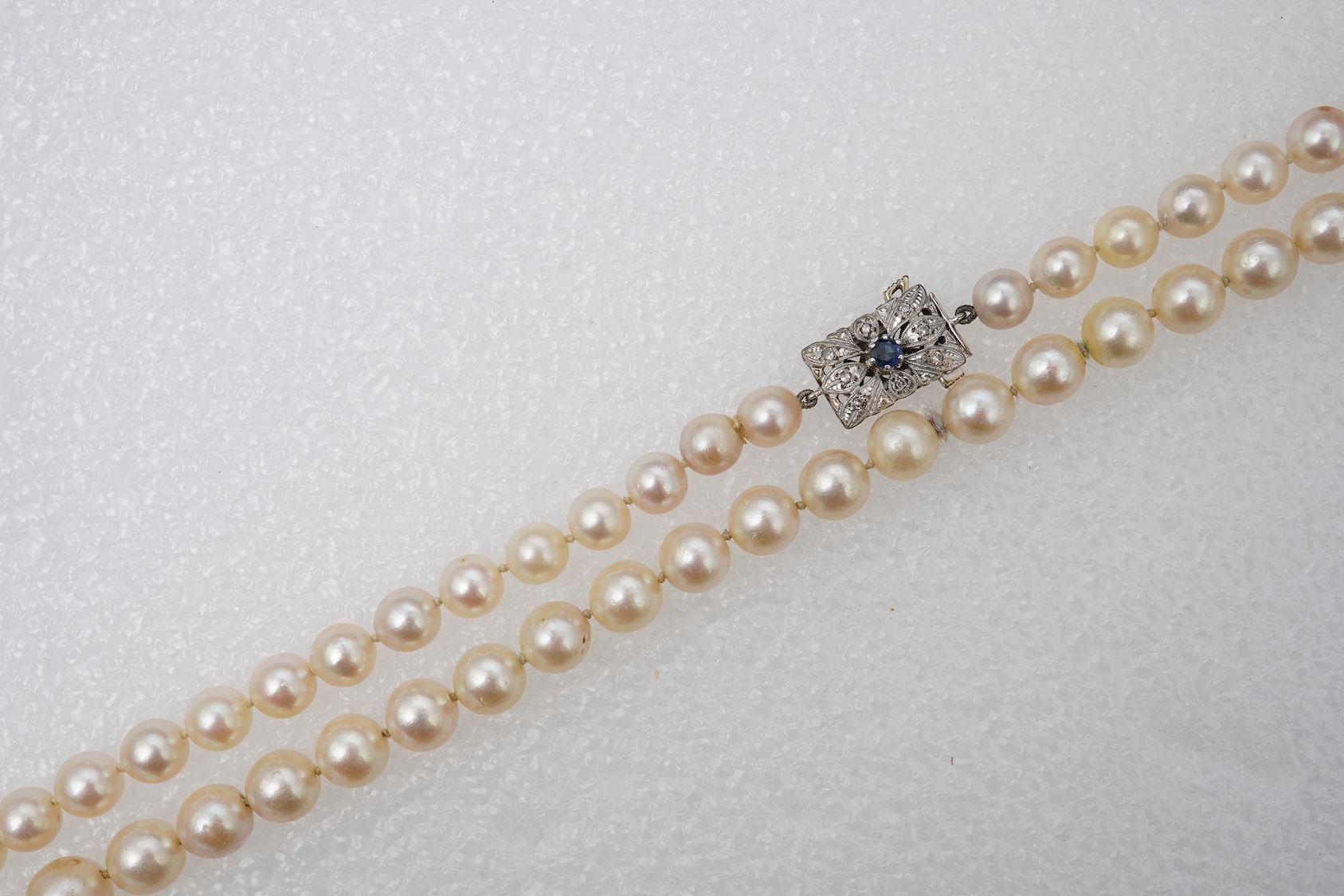 A cultured pearl, sapphire and diamond necklace, the single strand of graduated pearls measuring approximately 7.5-10.3mm, to a floral panel clasp in white gold, set with a circular-cut sapphire and brilliant-cut diamond